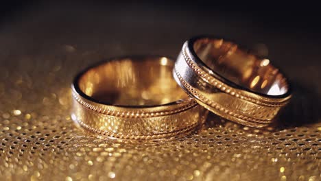 Wedding-rings-lying,-rotate,-spinning-on-shiny-golden-shining-surface-with-light,-close-up-macro