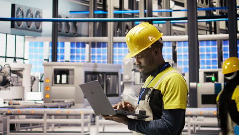 vertical video technician in solar panels factory oversees robot assembly lines using laptop