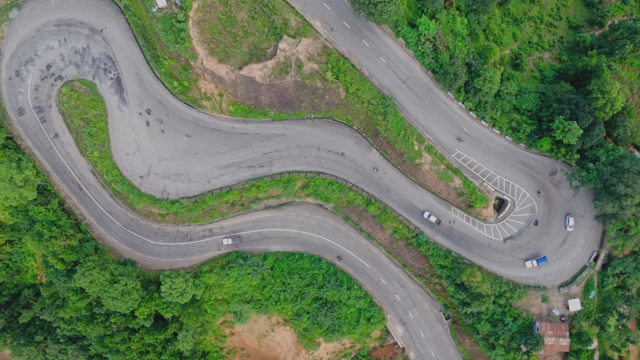 Aerial view of a vehicle driving along a winding hillside road surrounded by lush green mountains, showcasing scenic mountain travel, nature, and rural transportation beauty