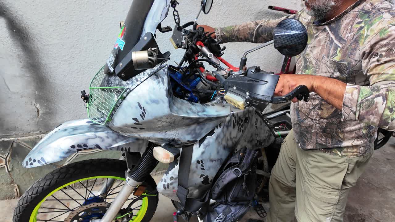 Pulling back from a mechanic's hands performing preventative maintenance on a white camouflage adventure motorcycle
