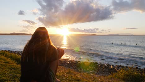 girl sitting and admiring golden sunset setting in the ocean - sunset at noosa national park in qld, australia