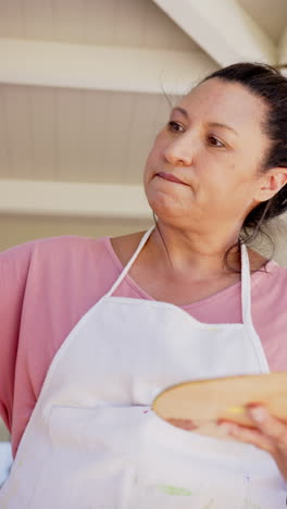 vertical video: painting on canvas, woman in apron focusing on her artwork