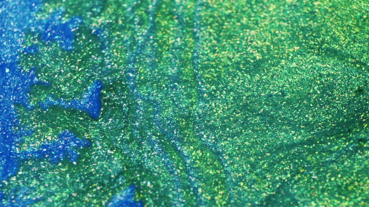 Macro shot of glittery green ink flowing through vivid blue pigment in liquid. Colorful, dynamic fluid motion