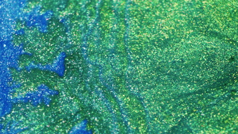 macro shot of glittery green ink flowing through vivid blue pigment in liquid. colorful, dynamic fluid motion