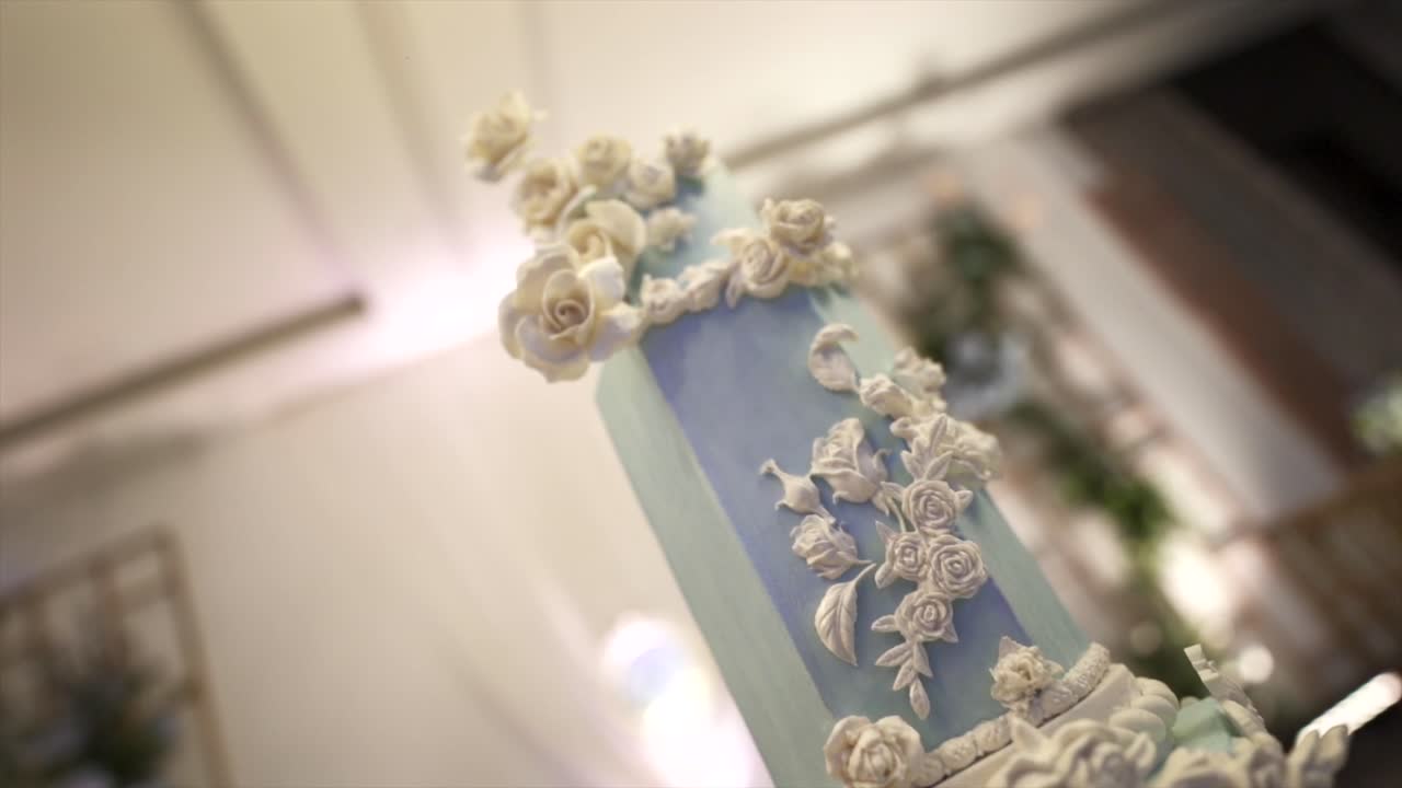 Downward close-up of an ornate blue and white wedding cake with white floral icing, with a second cake visible beside it