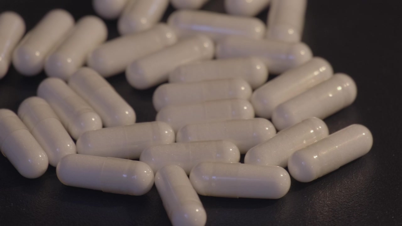 Capsule bianche di integratori alimentari sparse su uno sfondo scuro.