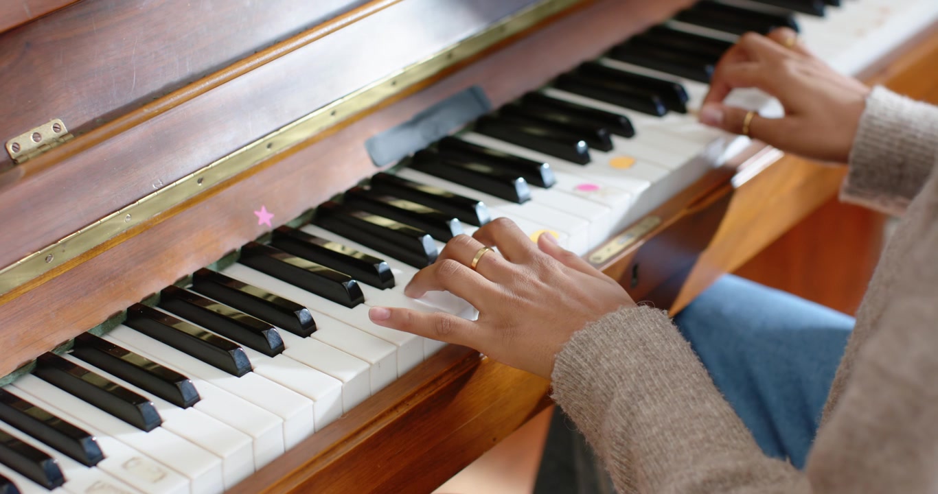 Mani che si posano sui tasti centrali e inferiori del pianoforte vicino alla finestra, premendo adesivi e facendo pratica