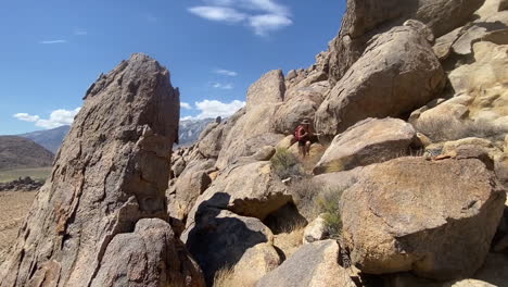 female with backpack on hiking trail in alabama hills, california usa on hot day walking on hill between rocks, panoramic full frame slow motion