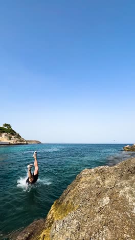 Static-vertical-shot-of-male-tourist-jump-and-dive-into-tropical-water,-Spain