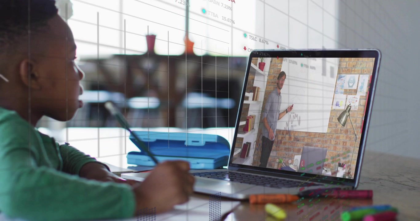 Boy writing homework at table, glancing at laptop while teacher starting lesson, charts overlaying