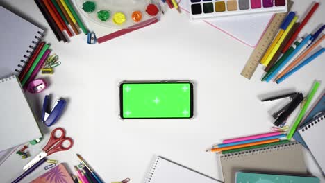 man put smartphone with chroma key in horizontal orientation on the table full of school supplies