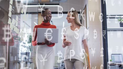 animation of currency symbols against two diverse women discussing over a laptop at office