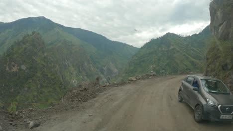 a point of view shot of a vehicle riding through dangerous and damaged dirt road carved through steep rocky cliff in the himalaya after the landslide