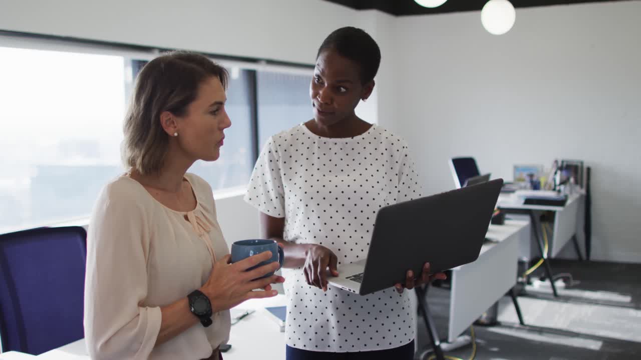 dos colegas femeninas diversas mirando la computadora portátil y discutiendo en la oficina