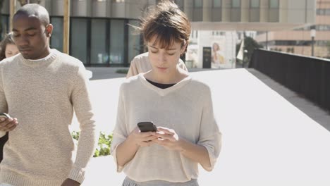 focused young citizens walking on street with phones