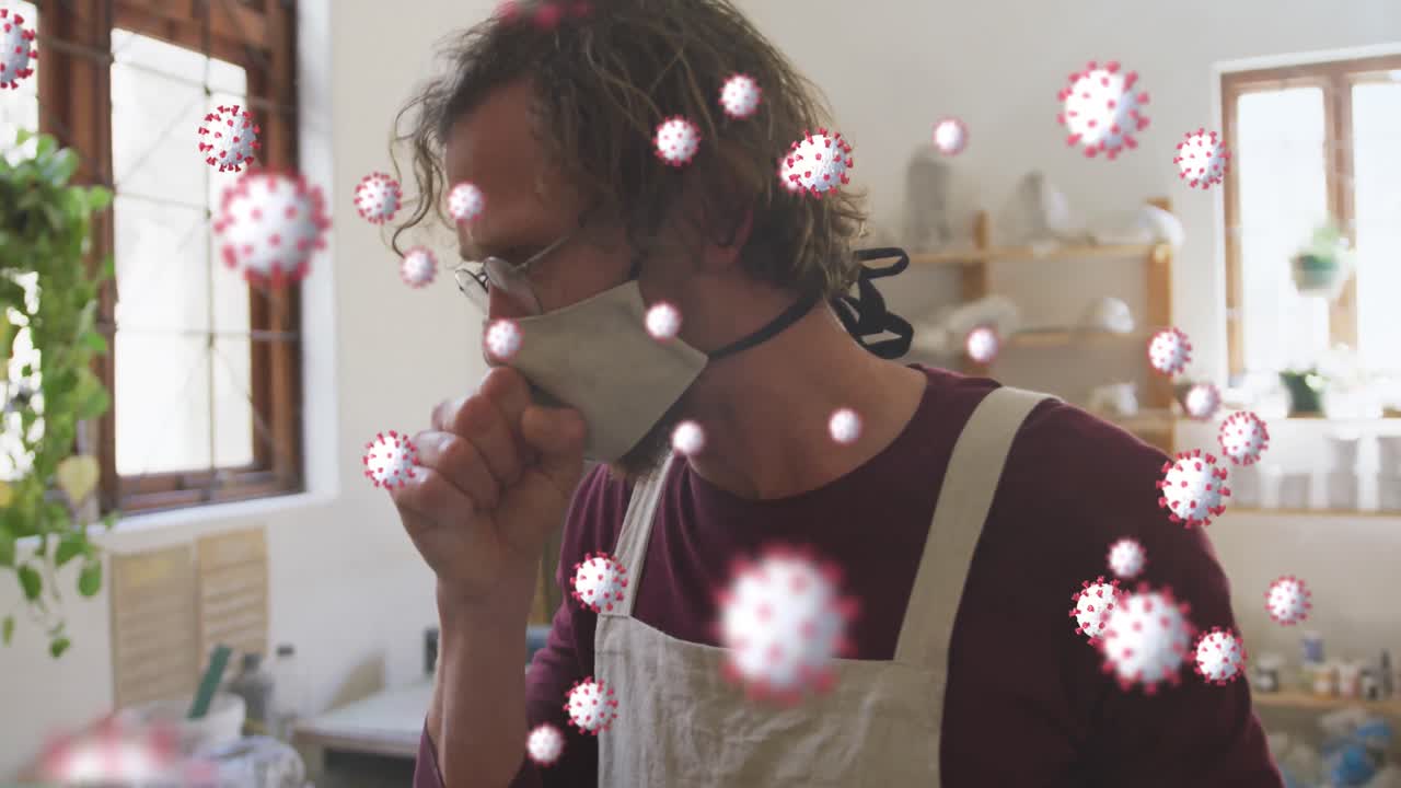 animación de células de coronavirus flotando sobre un hombre caucásico con máscara facial tosiendo en un taller de cerámica