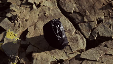 una bolsa de basura negra en una playa rocosa