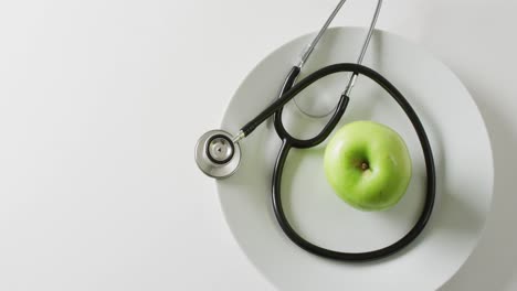 Video-of-stethoscope-with-apple-on-plate,-on-white-background-with-copy-space