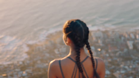 woman-on-mountain-top-looking-at-view-of-ocean-at-sunset-girl-standing-on-edge-of-cliff-enjoying-travel-freedom