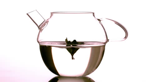 mint leaf falling into glass teapot