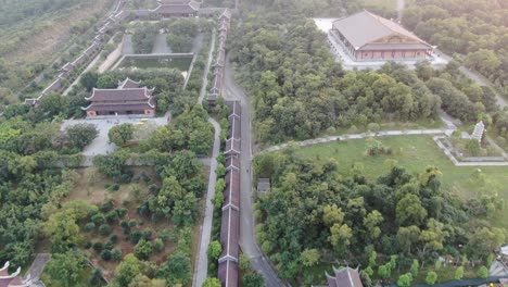 Drone-aerial-view-in-Vietnam-flying-over-buddhist-temple-area-with-pagodas-and-roads-covered-with-green-trees-in-Ninh-Binh-at-sunset