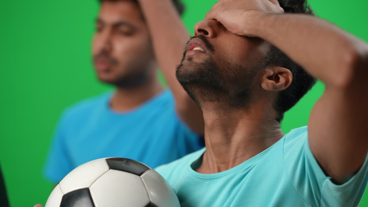 aficionado al fútbol concentrado en primer plano con la pelota viendo el partido haciendo una expresión facial decepcionada. amigo borroso de oriente medio sosteniendo la bandera alemana en el fondo en la pantalla verde. derrota del campeonato.