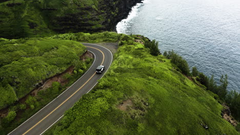 jeep drives around bend in maui mountain road, cliff and ocean below.