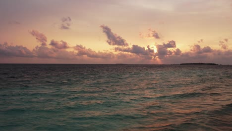 drone view of maldives sunset over calm ocean, panoramic pink sky and island