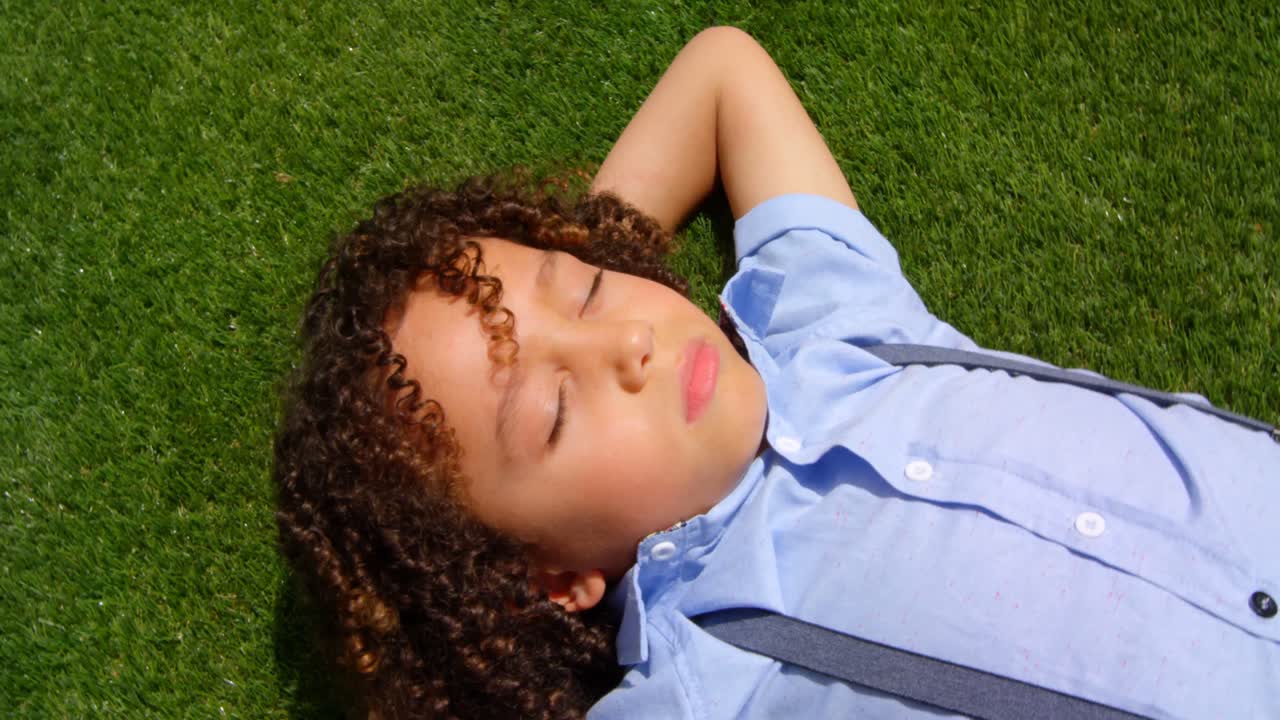 High angle view of mixed-race schoolgirl relaxing on grass in school playground in sunshine 4k