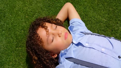 vista de alto ángulo de una colegiala de raza mixta relajándose en la hierba en el patio de recreo de la escuela en el sol 4k