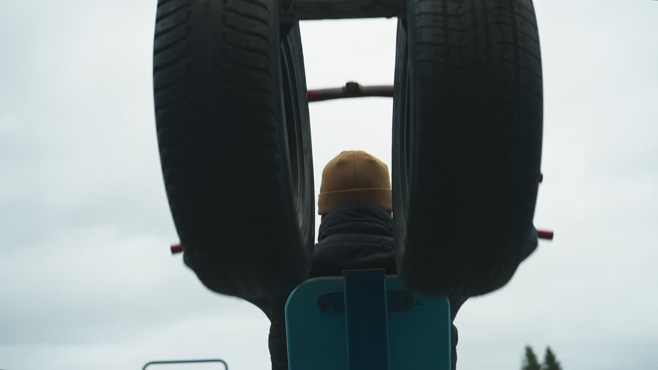 Back view of a coach doing pull-ups on a workout equipment, as he pauses and moves his neck side to side
