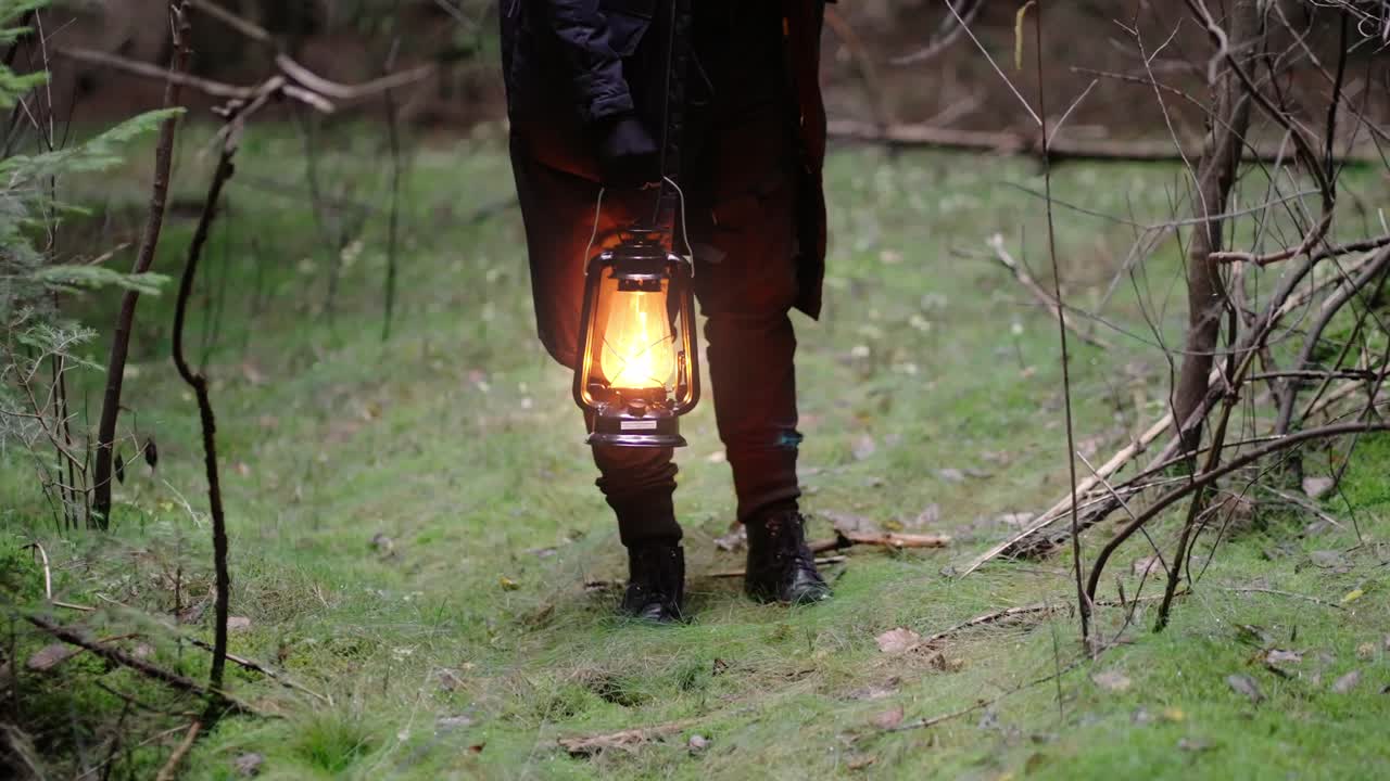 una figura sospechosa de negro encuentra una linterna de aceite ardiendo brillantemente en el bosque.