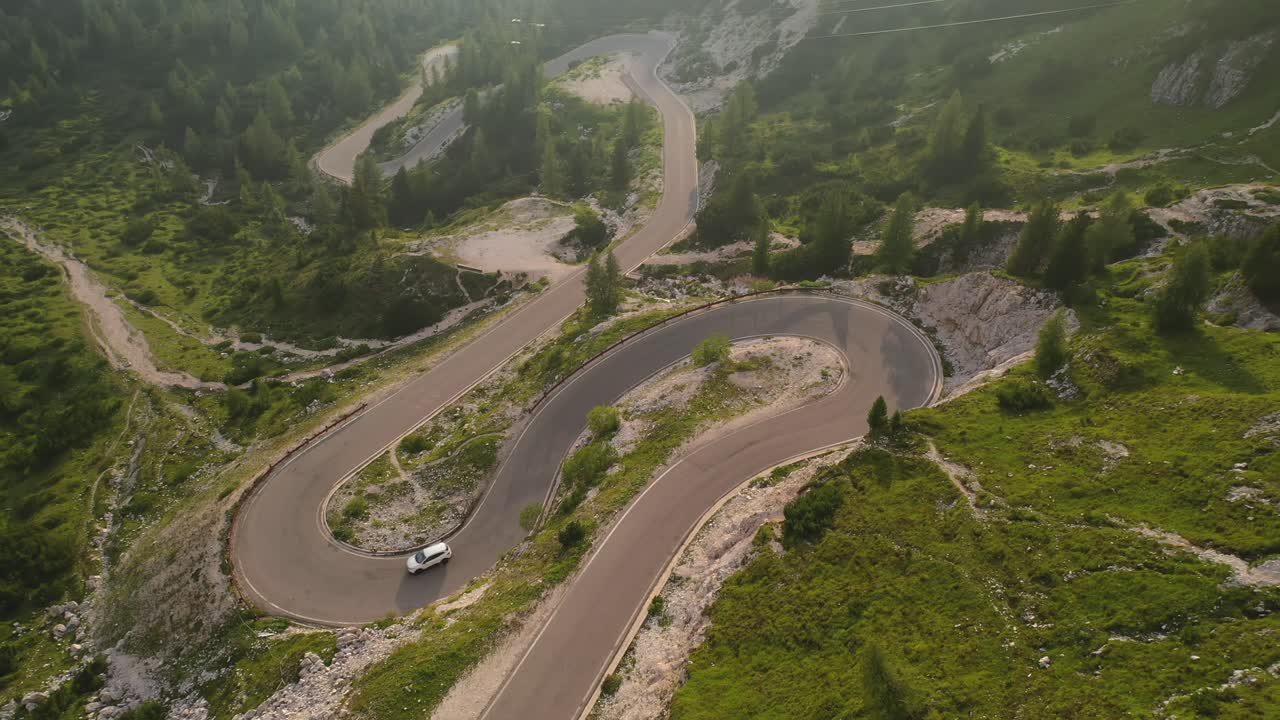 White car driving down winding mountain road in Italy, forward aerial