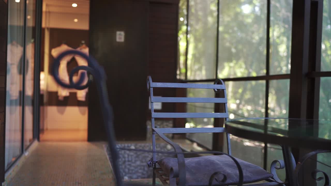 Cozy hotel room features a balcony with a metal chair and table, offering a peaceful view of a lush, forested area, perfect for relaxation and tranquility