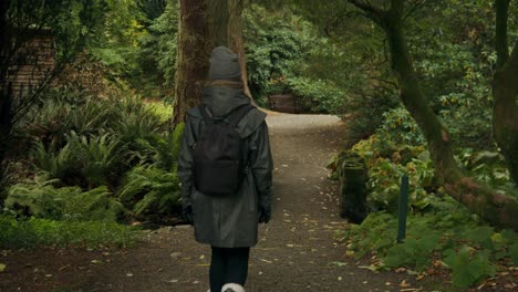 Female-hiker-walks-away-over-stone-bridge-in-autumnal-arboretum