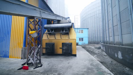 Modern elevator factory outdoors. A walk along the structures and under the long rectangular pipe. Aluminum cisterns at the backdrop of foggy sky.