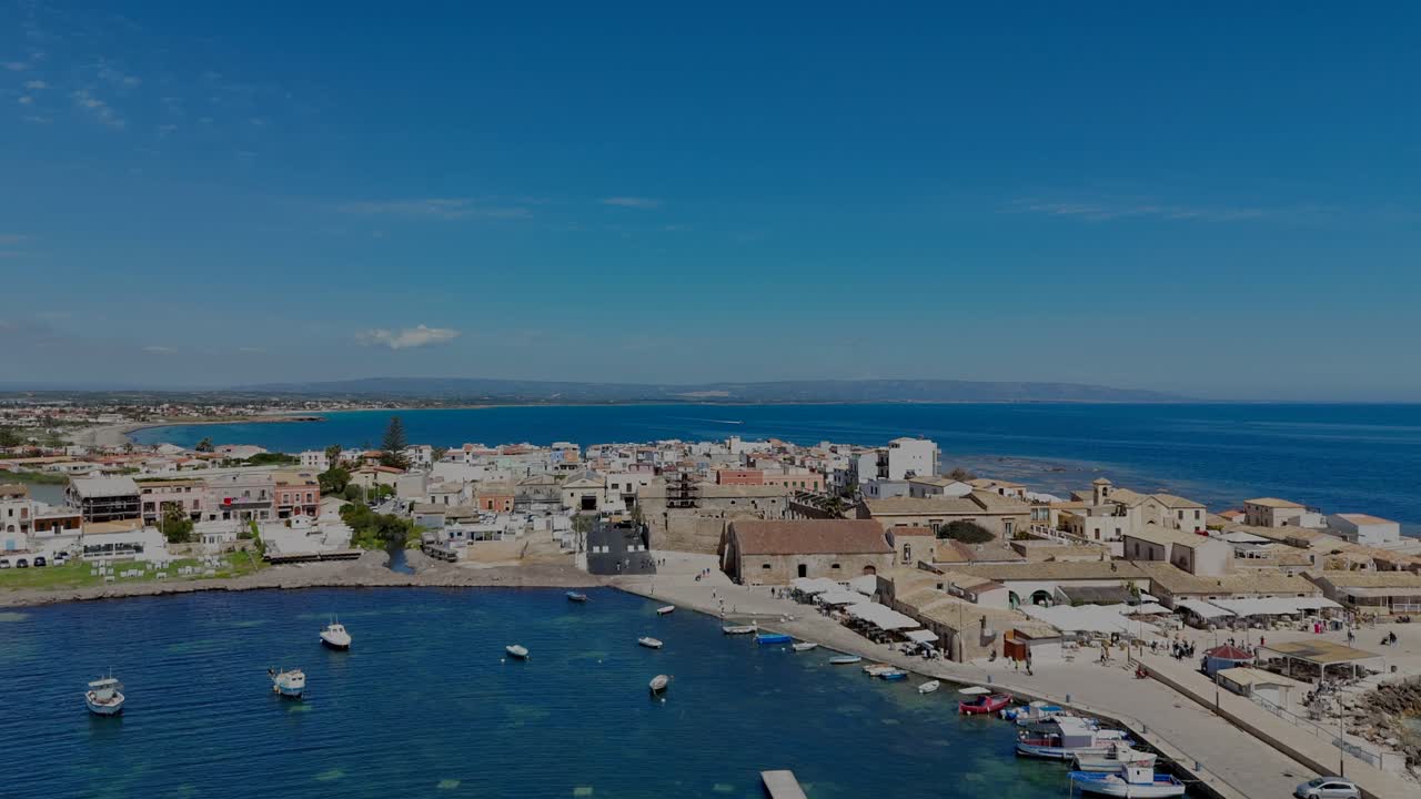 Drone flight horizontally on left side revealing the landscape behind Marzamemi village and the boats