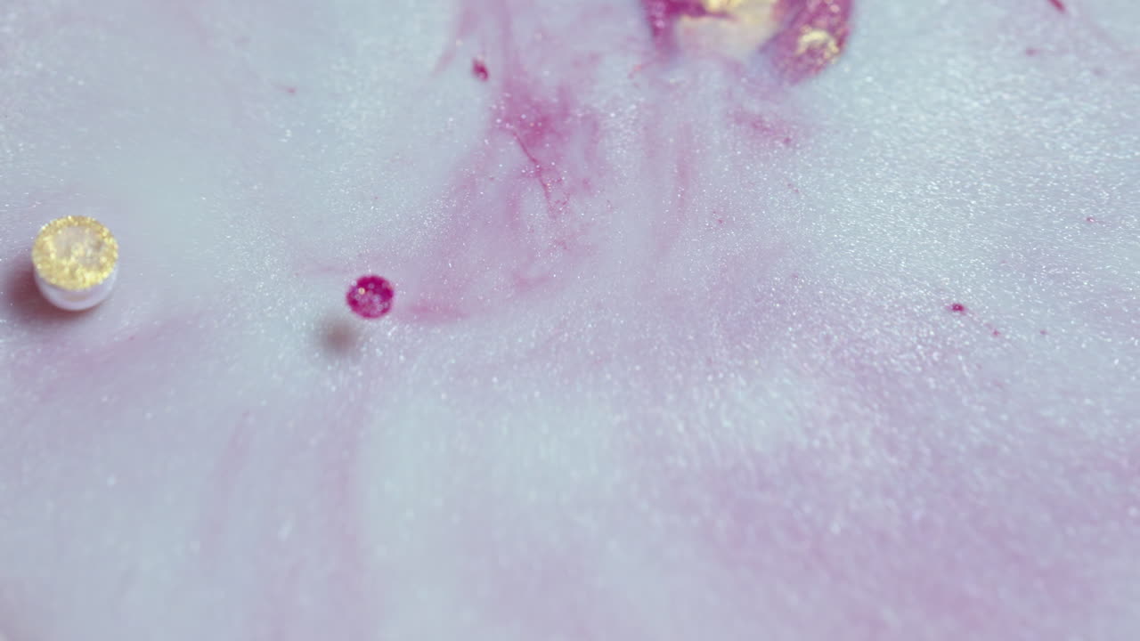 금색 반점이 있는 물 속에서 회전하는 분홍색 잉크의 클로즈업으로 추상적인 예술을 만니다.