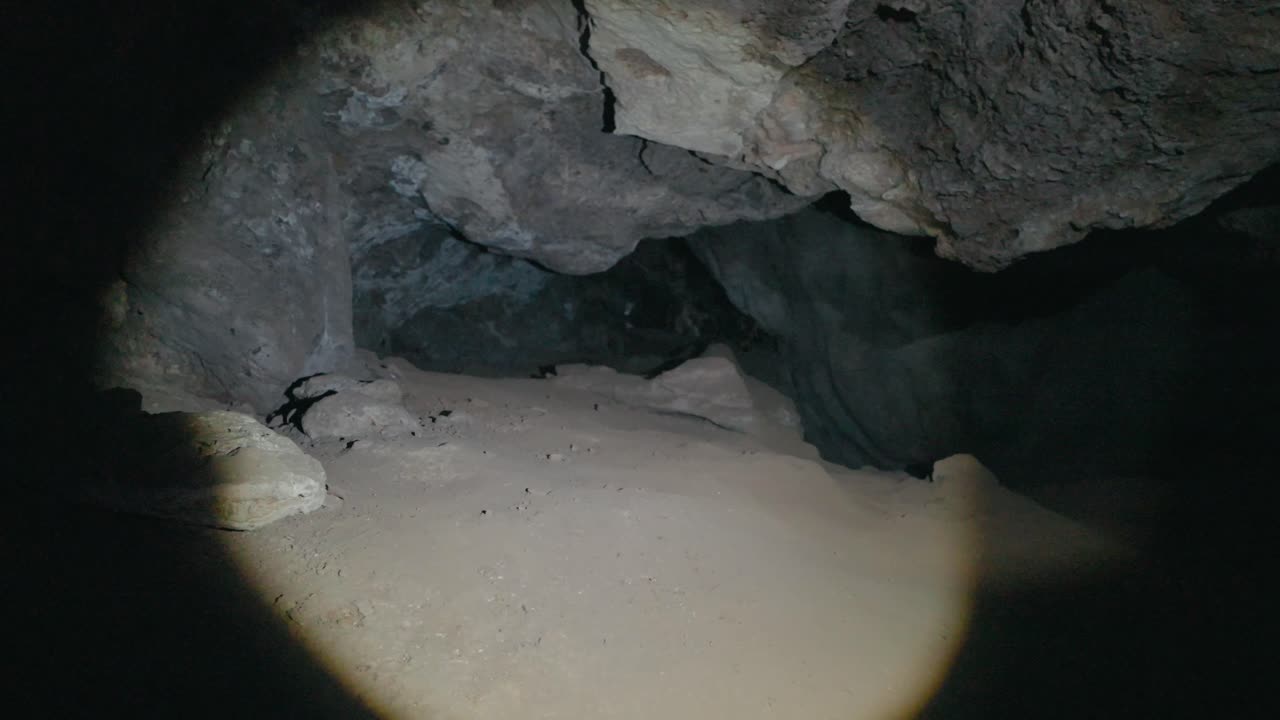 POV shot of a flashlight guiding through a dark cave. Textured rock walls and mysterious underground spaces create a dramatic, immersive exploration experience