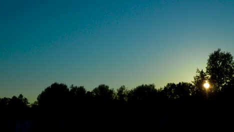 Zeitraffer-In-4K-Eines-Blauen-Und-Klaren-Abendhimmels,-An-Dem-Die-Sonne-Hinter-Bäumen-Untergeht