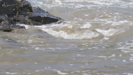 waves roll up and down a beach rock, carrying along sand and gravel