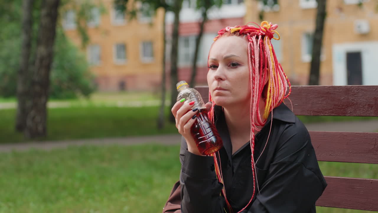 Una mujer con rastas interrumpe su paseo, una mujer con trenzas rojas brillantes se detiene pensativa mientras bebe algo durante su paseo, una mujer con rastas y un pelo rojo vibrante se toma un momento para reflexionar durante su paseo