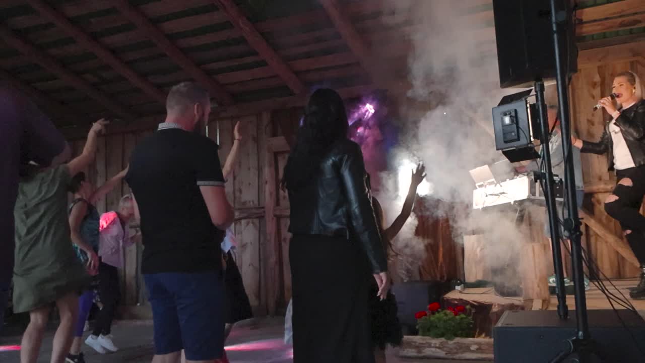 People listening to a local band called Kurjad Plaanid in a barn during summer time while smoke comes out of the machine and strobe and spot lights light up the room in slow motion. Artist is jumping.