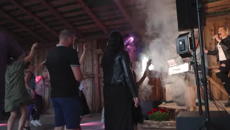 people listening to a local band called kurjad plaanid in a barn during summer time while smoke comes out of the machine and strobe and spot lights light up the room in slow motion. artist is jumping.