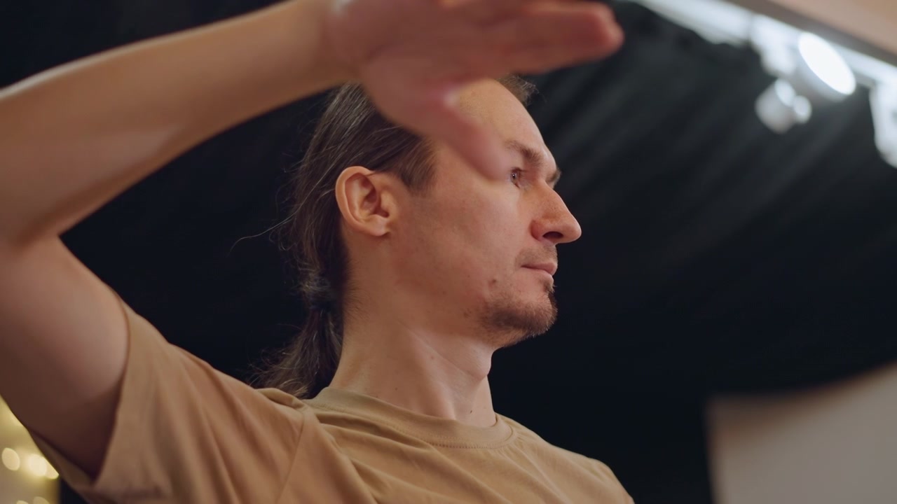 Director de orquesta caucásico dirigiendo un ensayo con gestos expresivos de las manos y perfil concentrado, ambiente íntimo de masterclass en estudio, enseñando técnica a estudiantes, iluminación escénica sutil, casual.