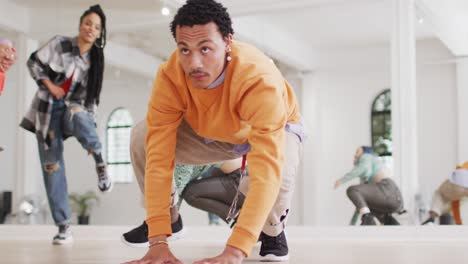 bailarín masculino biracial estirándose con diversos colegas en un estudio de baile, cámara lenta