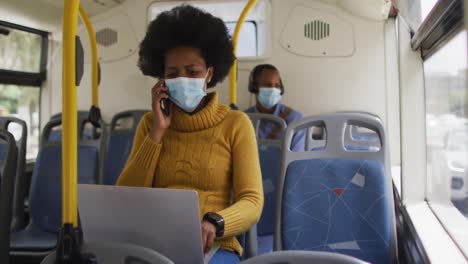 Afroamerikanische-Geschäftsfrau-Mit-Gesichtsmaske,-Die-Auf-Dem-Smartphone-Spricht-Und-Im-Bus-Sitzt