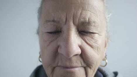 Senior-caucasian-lady-looks-at-camera-wrinkles-closeup-blinking-blue-eyes-white-hair-with-earrings-and-sports-wear,-face-portrait