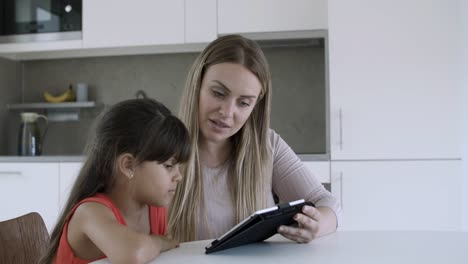 mamá mostrando el contenido de la tableta a la hija pequeña