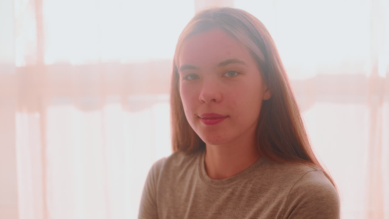 Lady seated close to window focusing on something then lifting head with confident look as natural light streams into room through curtain creating soft warm glow around her silhouette and profile
